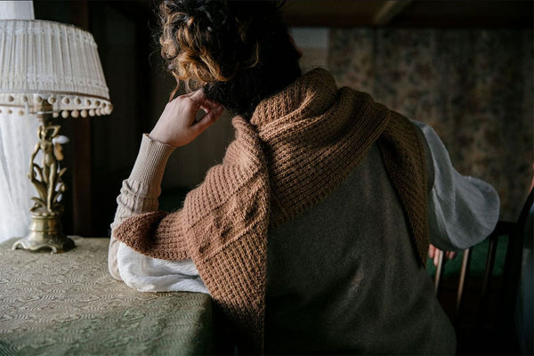 brown shawl wrapped around a person who has their back to the camera and is sitting at a desk