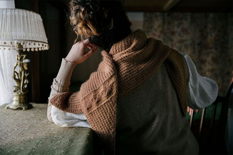 brown shawl wrapped around a person who has their back to the camera and is sitting at a desk