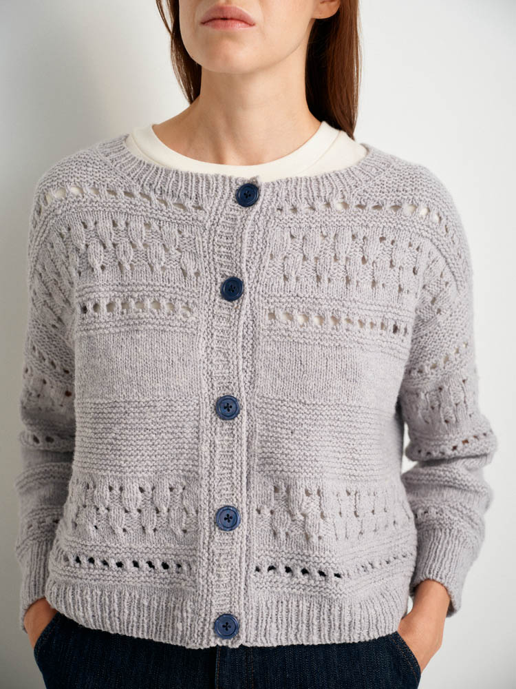Woman wearing a gray knitted cardigan with blue buttons on a white background