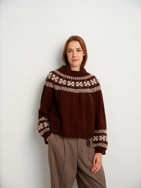 Person wearing a brown sweater with white patterns against a plain background