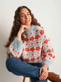 Woman wearing a floral sweater sitting on a chair against a plain background