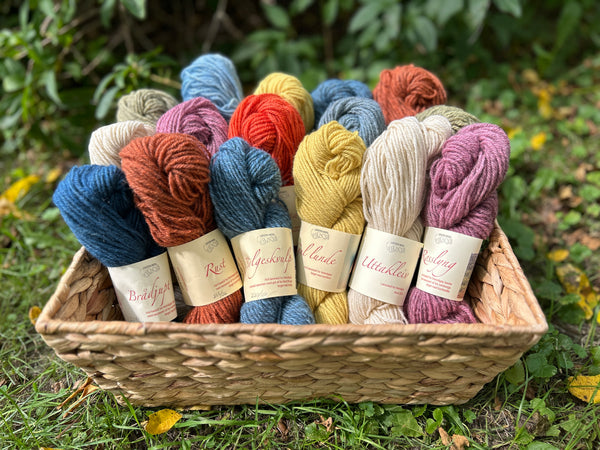 Basket of various coloured skeins of Lofoten Wool 3 ply outside on grass