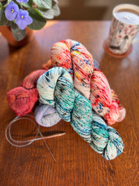 4 beautiful skeins of Malabrigo Arroyo on a table with a tea cup and a flowering potted plant in the background