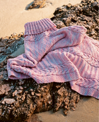 Marigold Poncho knit in Malabrigo Arroyo in the colourway Rosalinda laying on a beach