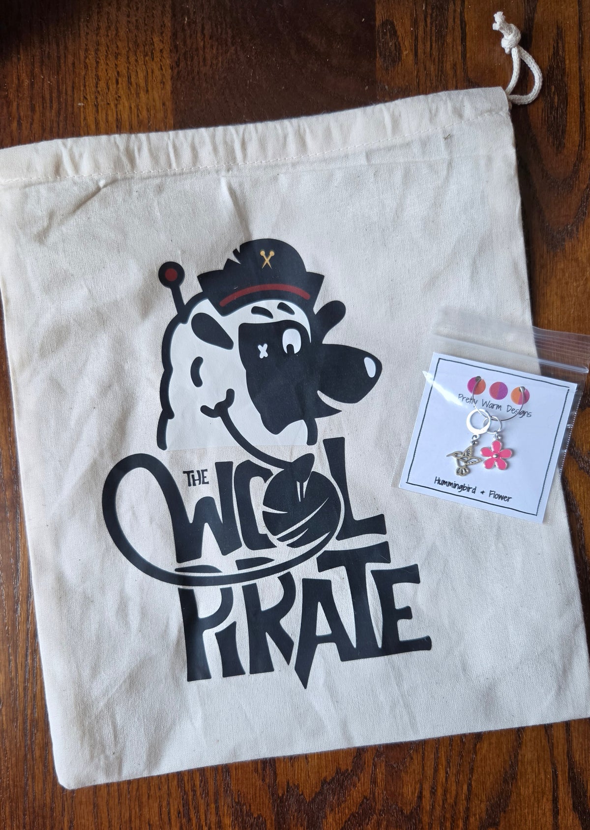 10 x 12" cotton muslin project bag with The Wool Pirate logo on the front and a stitch marker shown with it