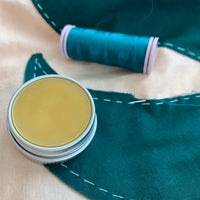 piece of teal fabric with visable stitch lines and an open tin of thread gloss