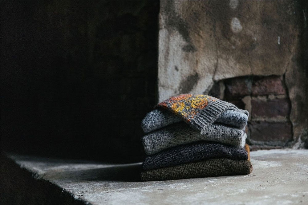 a stack of colourwork sweaters folded in a room