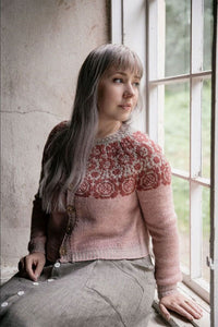 a woman wearing a colourwork yoke cardigan sitting in front of a window