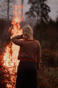 Person standing in front of a large bonfire with trees in the background