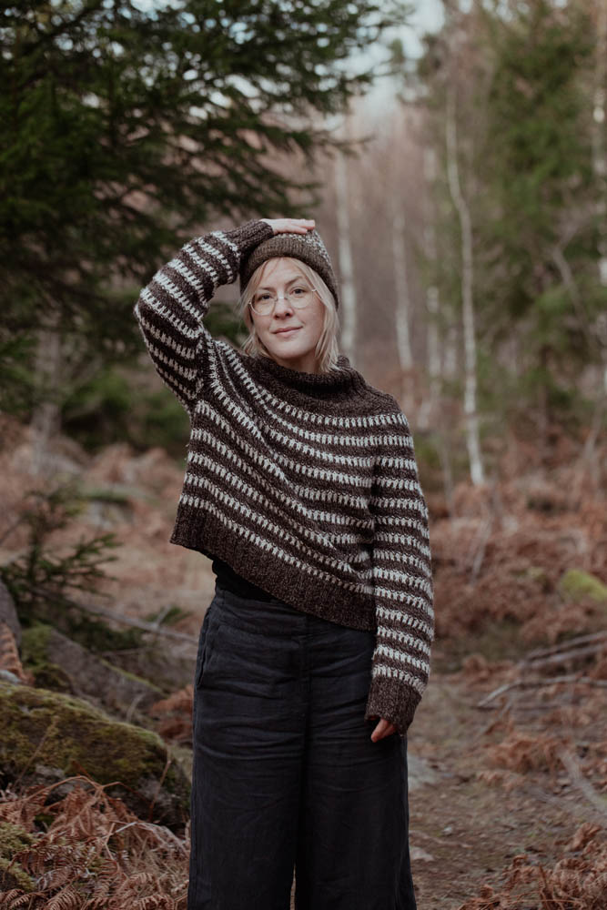 Person wearing a patterned sweater and beanie in a forest setting