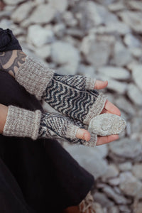Person wearing knitted fingerless gloves with a pattern, sitting on a rocky surface.