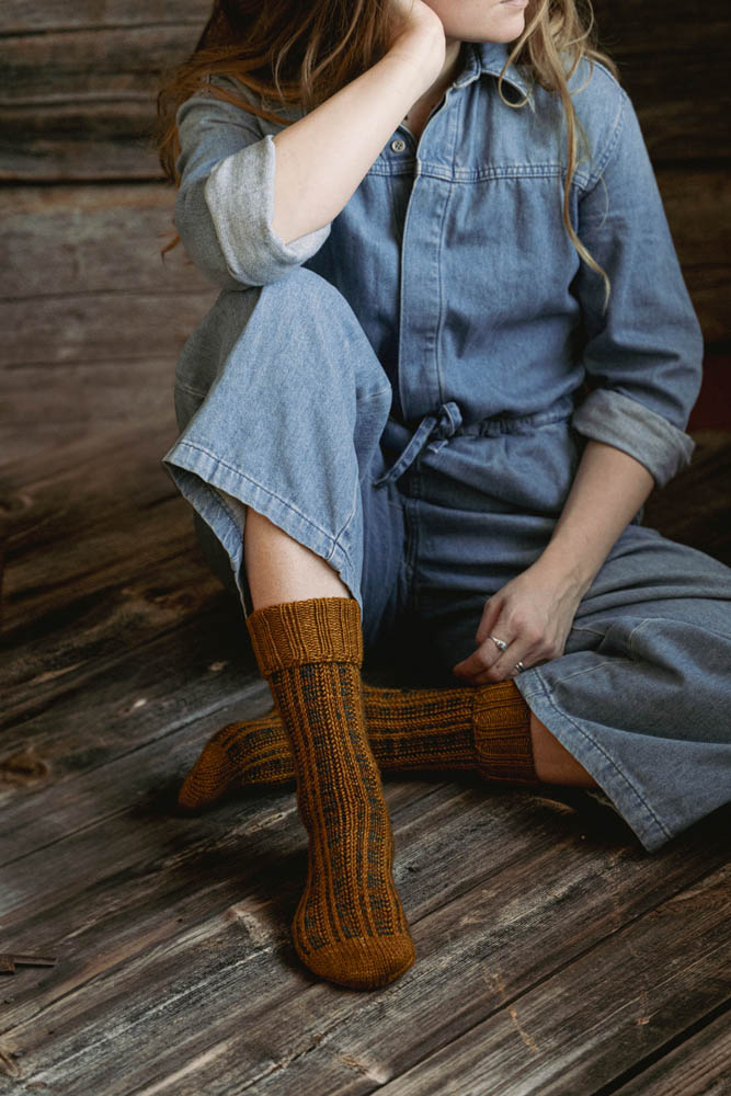 image of knit socks being worn on a woman sitting on the floor.  you can only see her from the chin down.