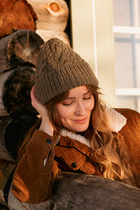 image of a knit hat being worn on a woman sitting outside by a log house.  