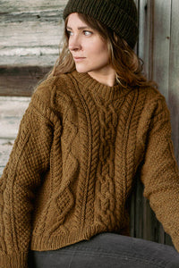 image of a woman wearing a cable knit sweater with a knit hat outside in front of wood wall