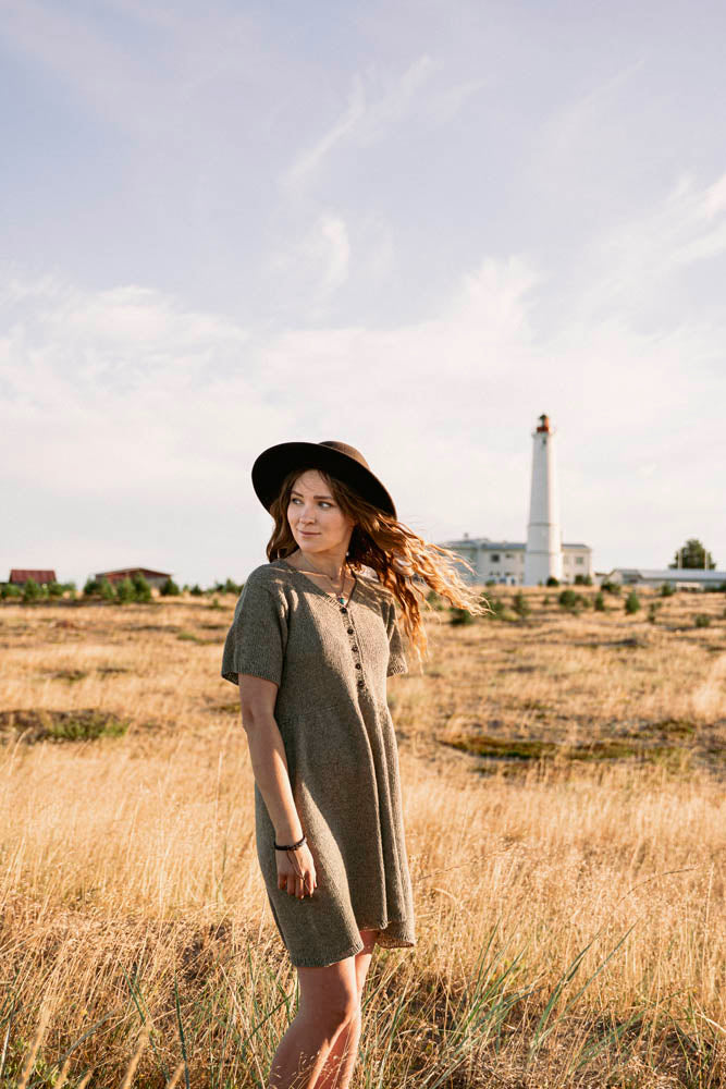 image of a woman in a knit dress out in a wild grass field with a lighthouse back in the distance.