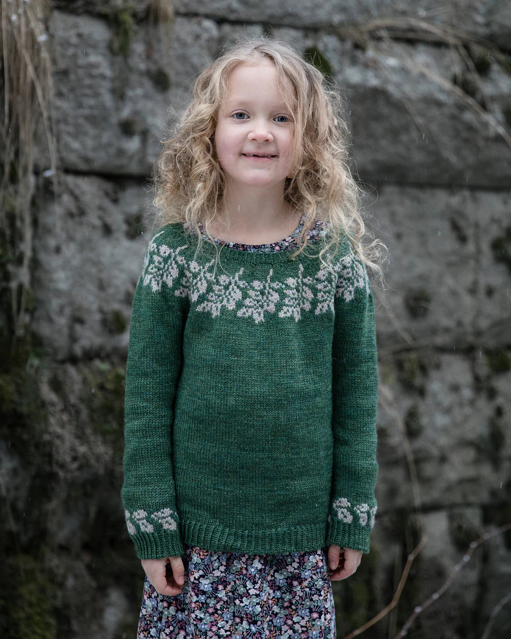 a child wearing a colourwork sweater standing in front of a stone wall