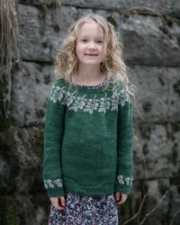 a child wearing a colourwork sweater standing in front of a stone wall