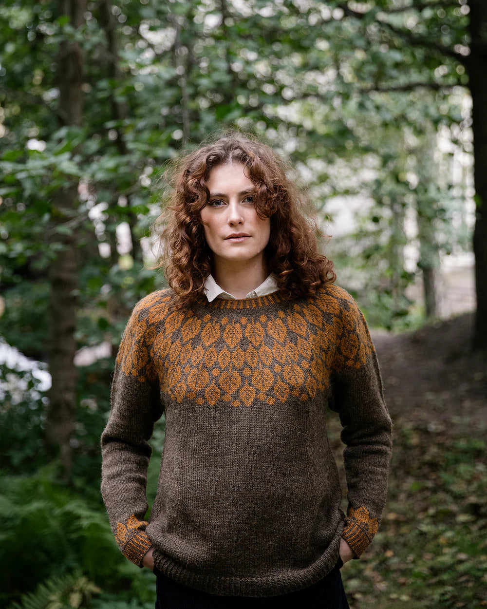 the designer wearing another colourwork sweater in a forest